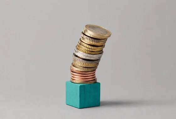 Monedas de euro apiladas en desequilibrio junto a un cubo, ilustración sobre cómo detectar el sobreendeudamiento